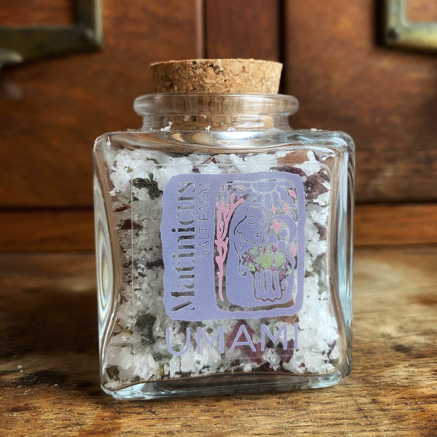 3 ounce glass jar containing sea salt mixed with sugar kelp and dulse seaweeds with cork lid on a wooden surface