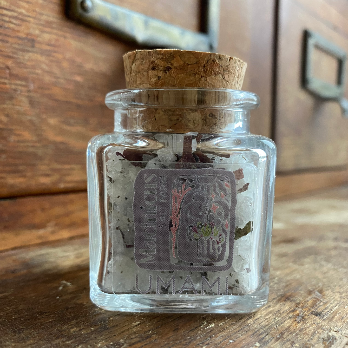 1.4 ounce glass jar containing sea salt mixed with sugar kelp and dulse seaweeds with cork lid on a wooden surface