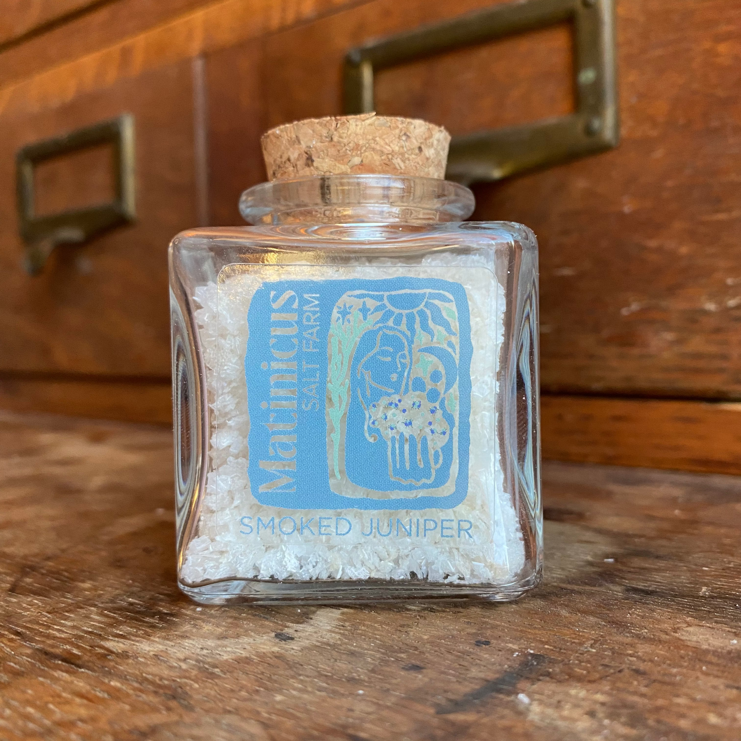 3 ounce glass jar containing smoked juniper sea salt with cork lid on a wooden surface