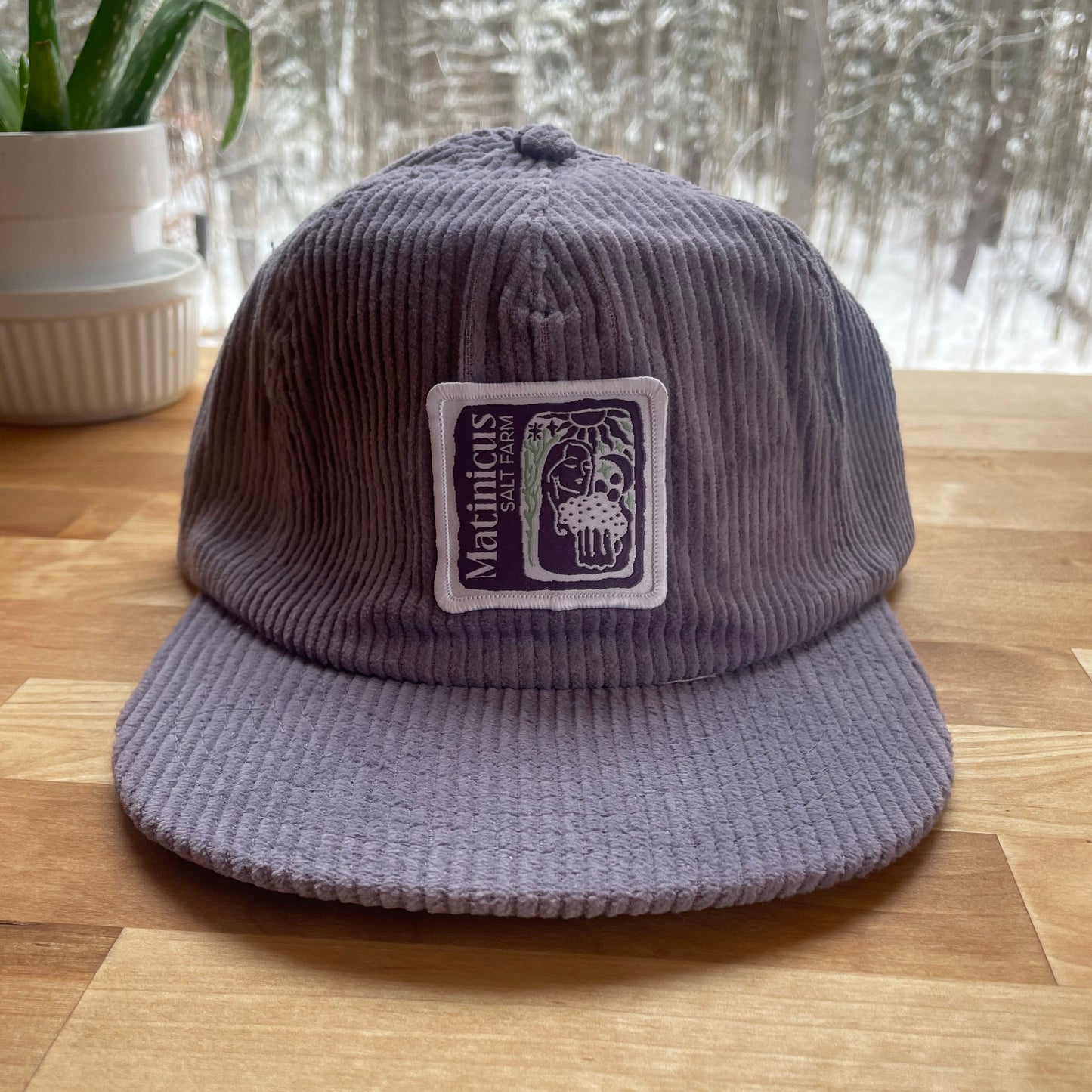 Purple corduroy cap with an indigo logo patch on a wooden surface