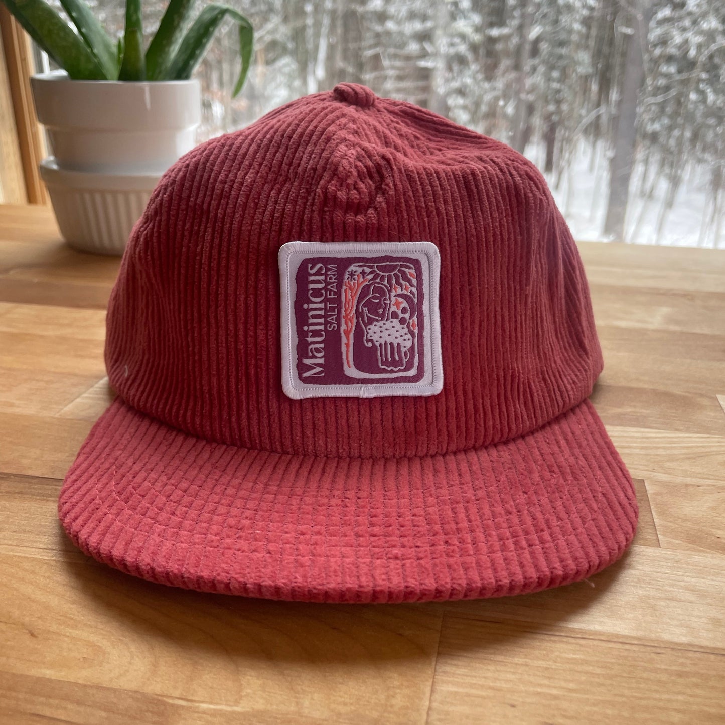 Red corduroy cap with a plum logo patch on a wooden surface