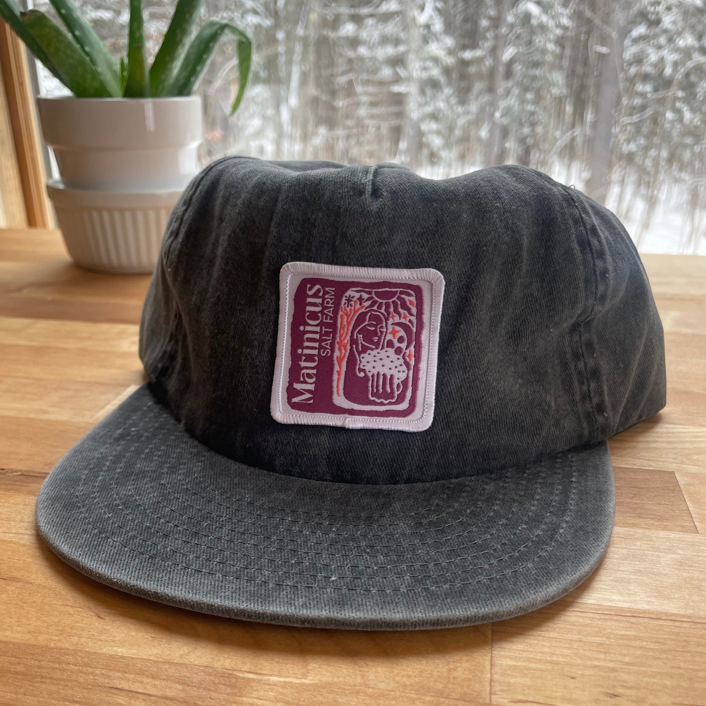 Black washed cotton cap with a plum logo patch on a wooden surface