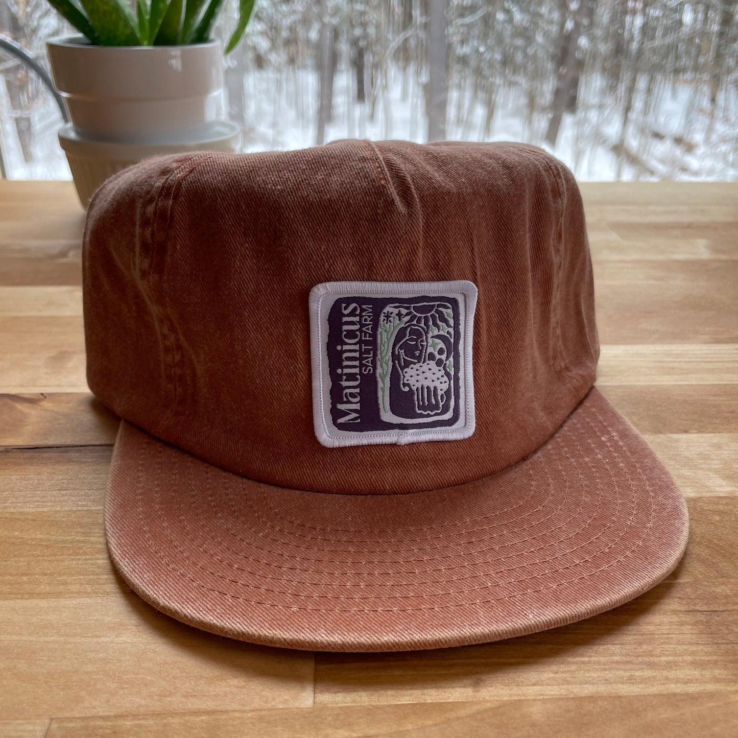 Orange washed cotton cap with an indigo logo patch on a wooden surface