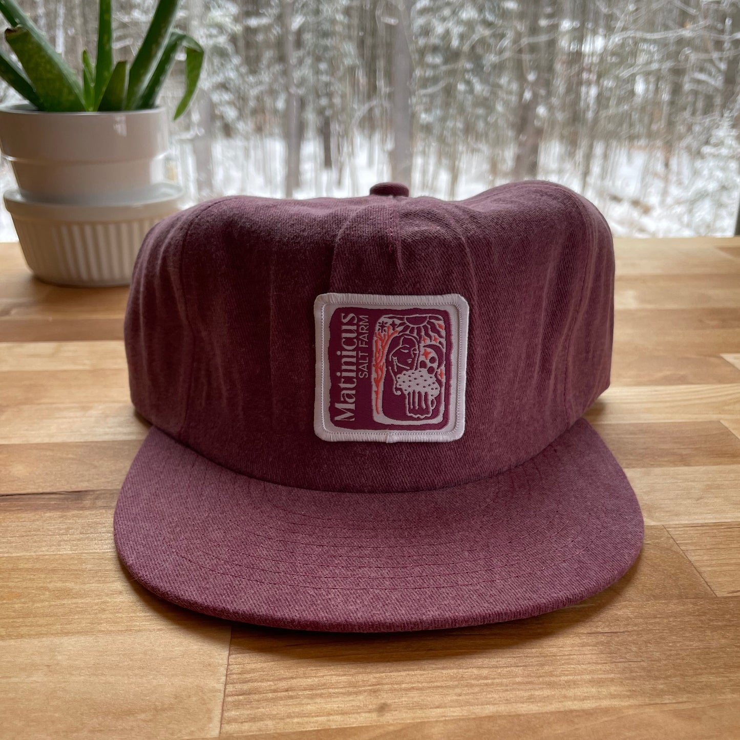Maroon washed cotton cap with a plum logo patch on a wooden surface