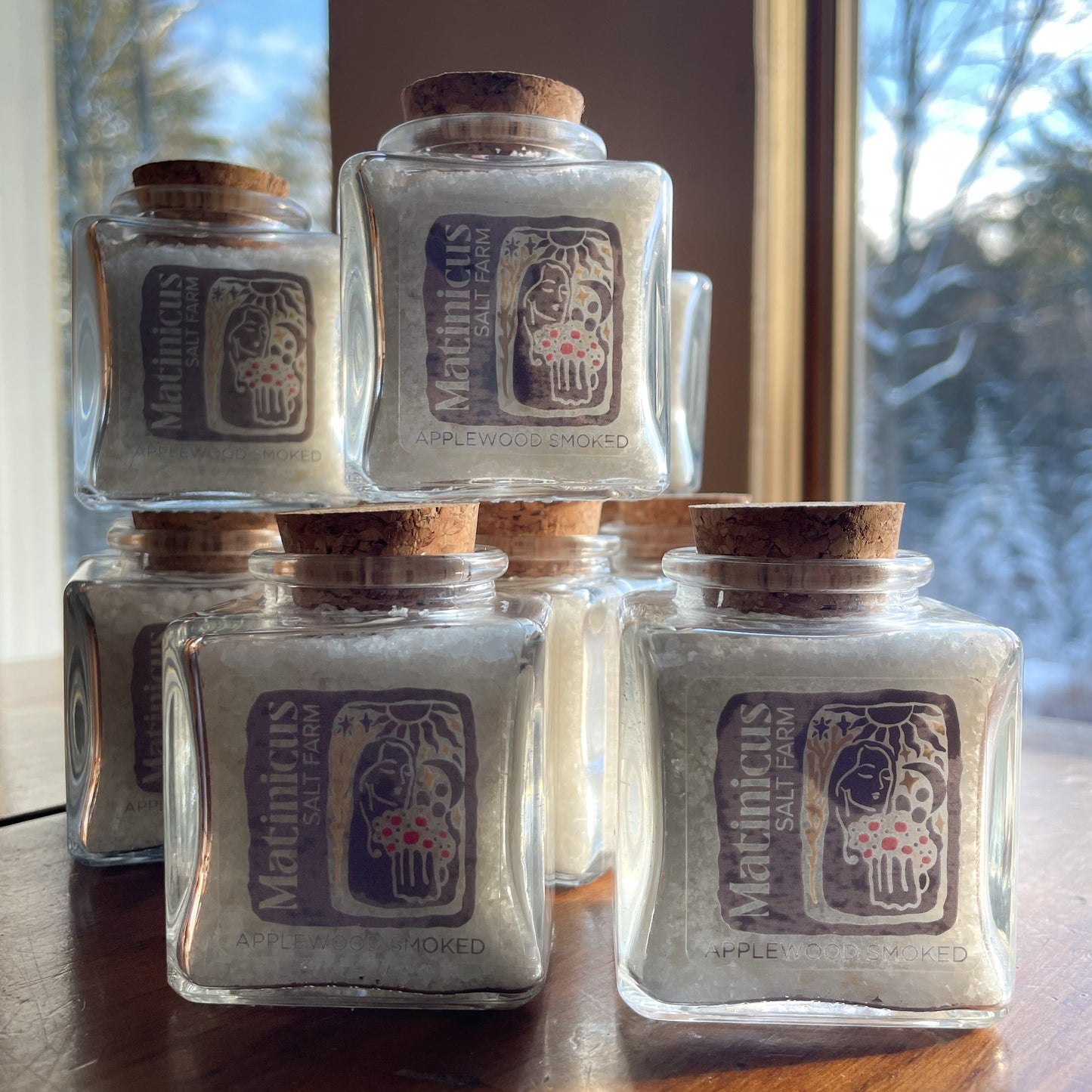3 ounce glass jars containing applewood smoked sea salt with cork lid stacked on a wooden surface
