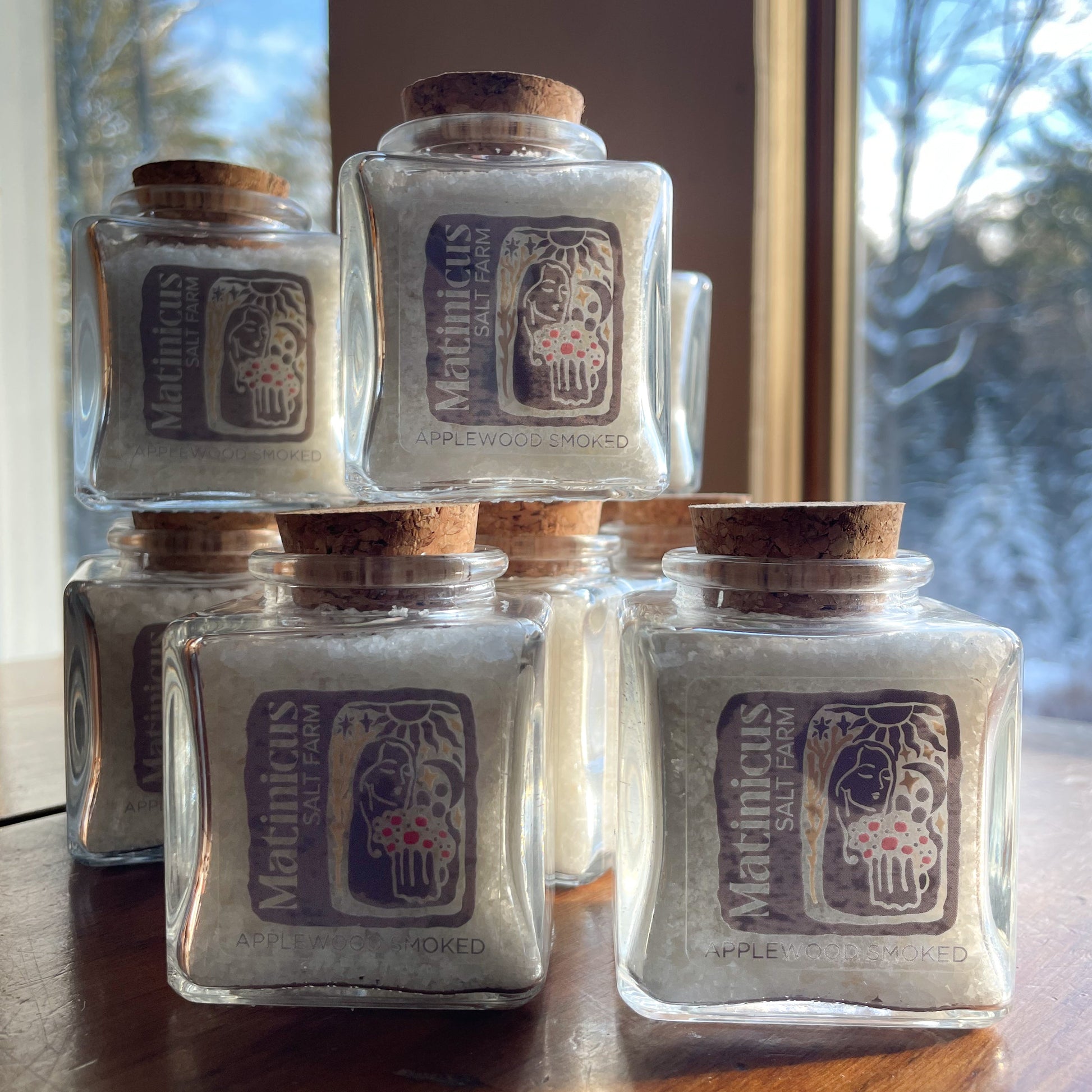 3 ounce glass jars containing applewood smoked sea salt with cork lid stacked on a wooden surface