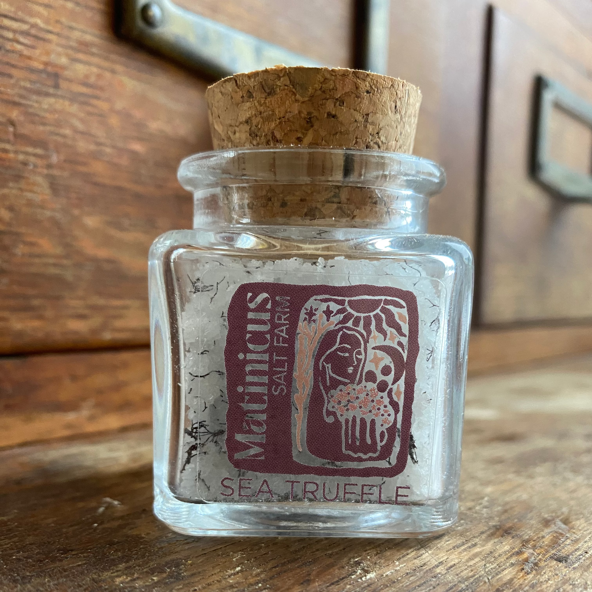 1.4 ounce glass jar containing sea salt mixed with truffle seaweed with cork lid on a wooden surface