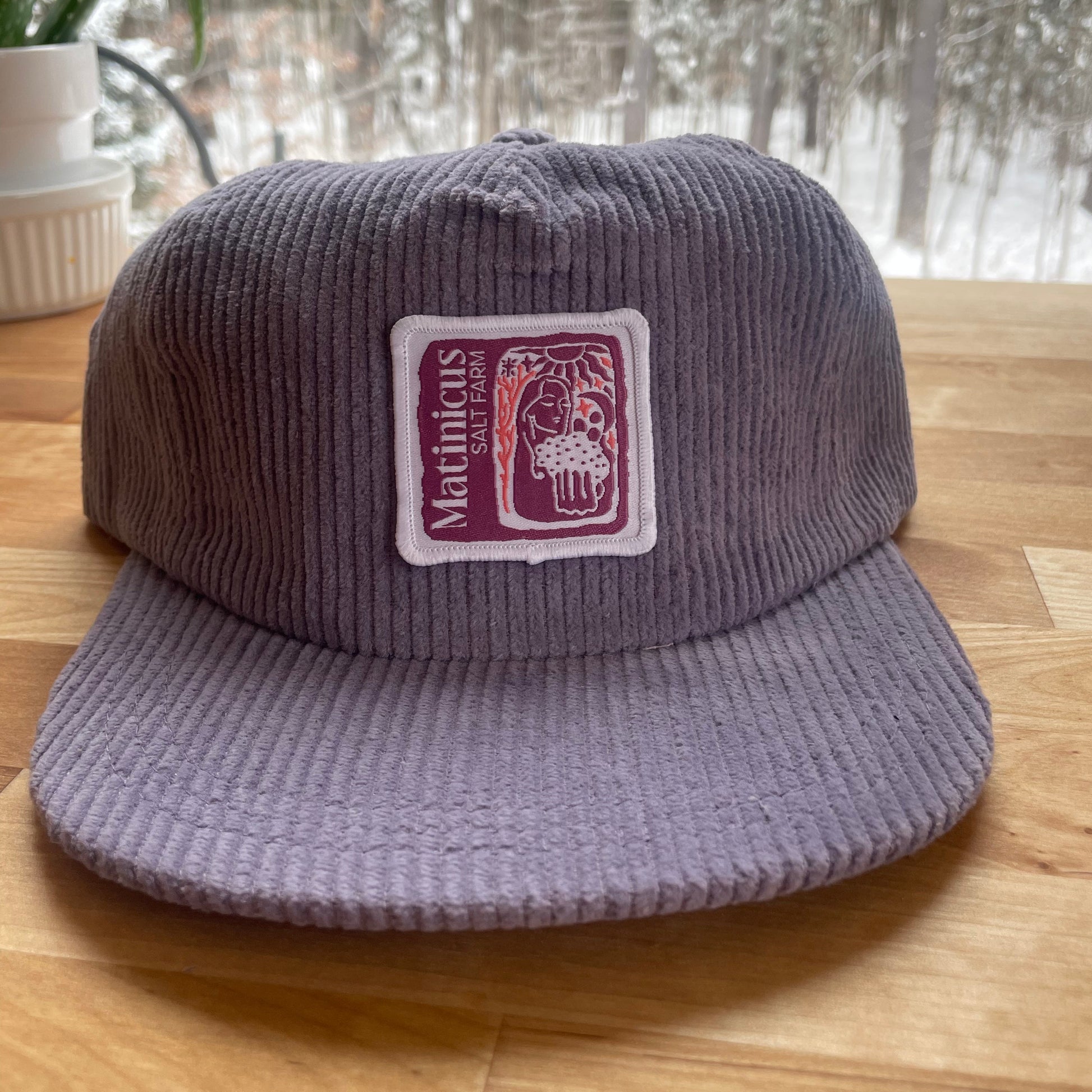 Purple corduroy cap with a plum logo patch on a wooden surface