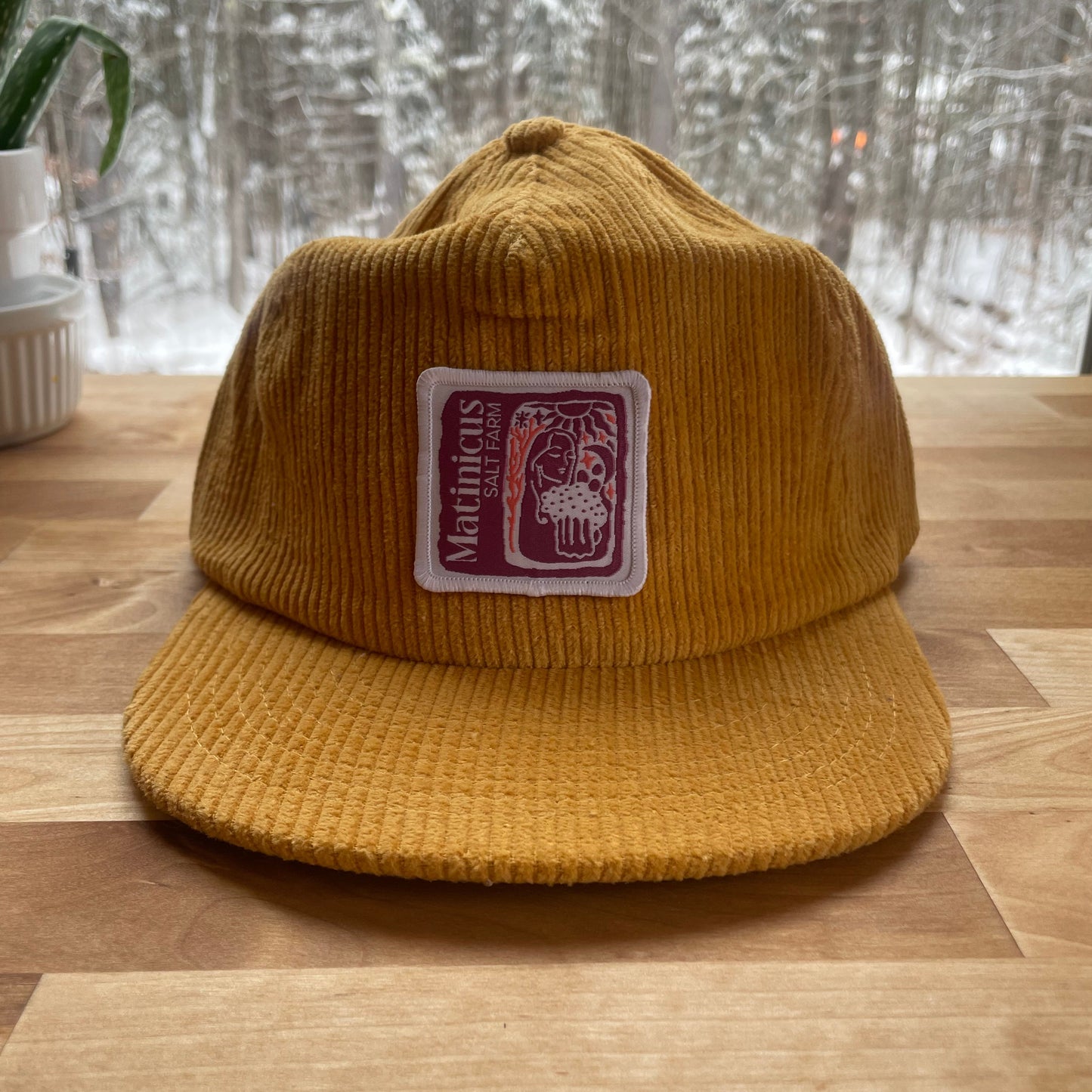 Yellow corduroy cap with a plum logo patch on a wooden surface