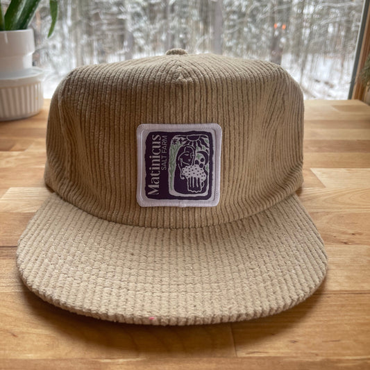 Beige corduroy cap with an indigo logo patch on a wooden surface