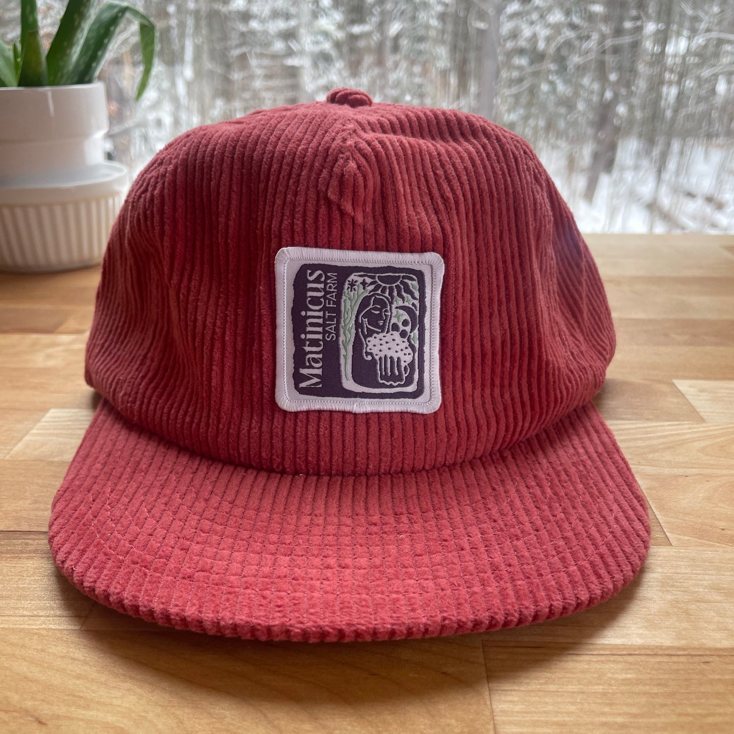 Red corduroy cap with an indigo logo patch on a wooden surface