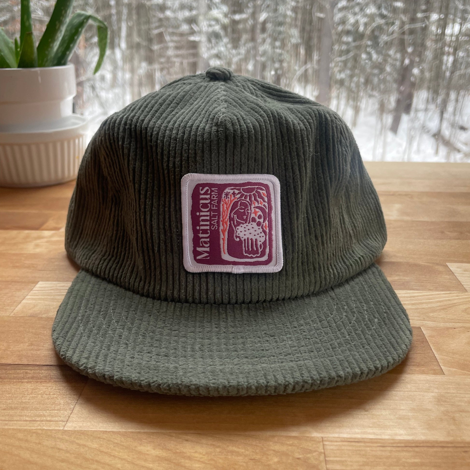 Green corduroy cap with a plum logo patch  on a wooden surface