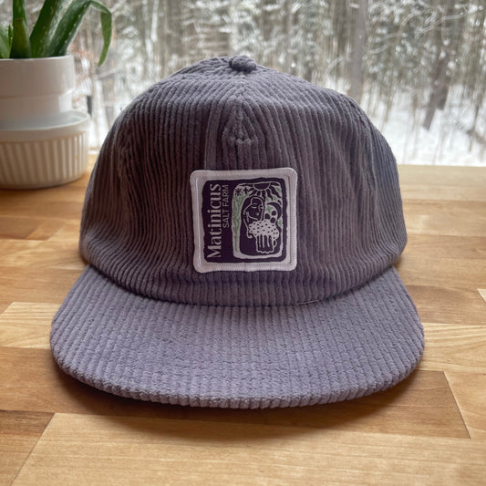 Purple corduroy cap with an indigo logo patch on a wooden surface
