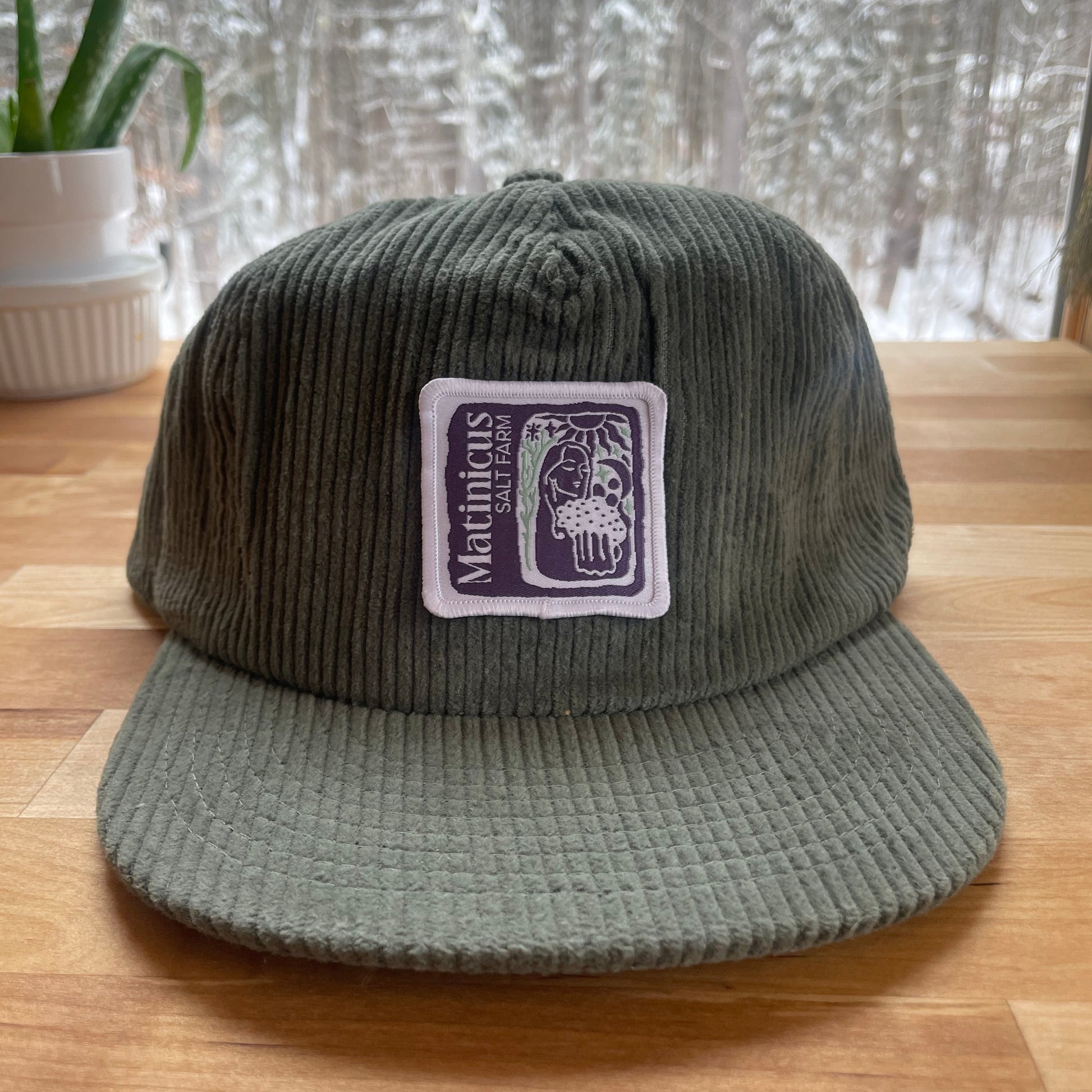 Green corduroy cap with an indigo logo patch on a wooden surface