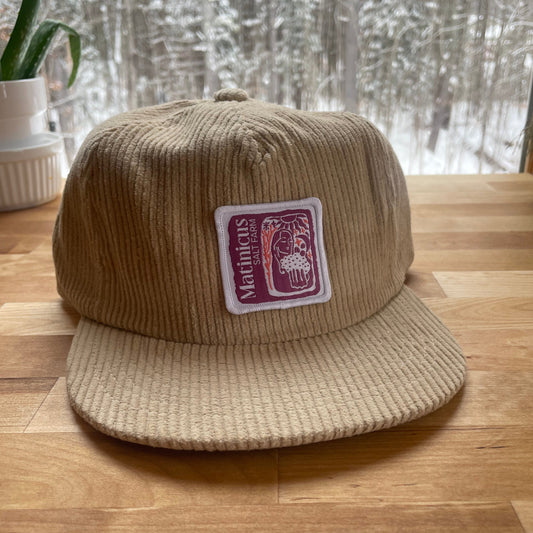 Beige corduroy cap with a plum logo patch on a wooden surface