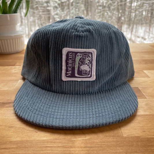 Blue corduroy cap with an indigo logo patch on a wooden surface