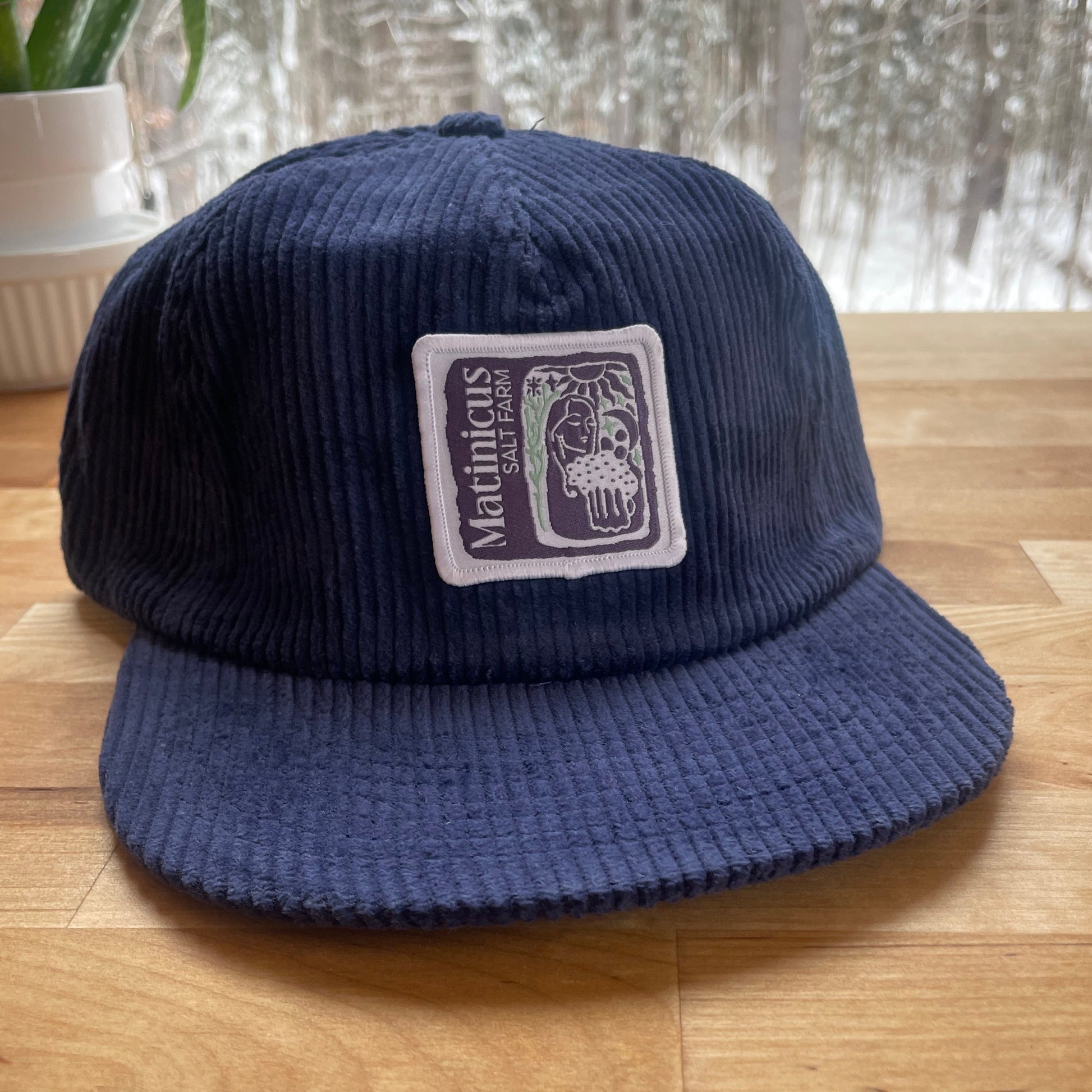 Navy blue corduroy cap with an indigo logo patch on a wooden surface