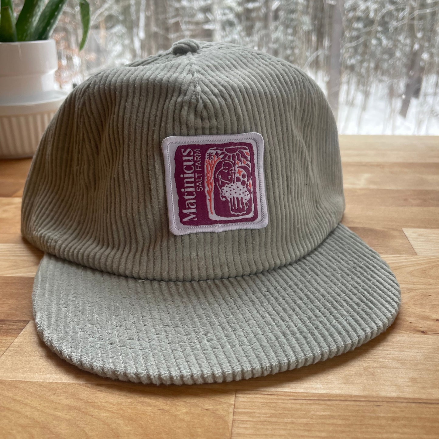 Gray corduroy cap with a plumb logo patch on a wooden surface
