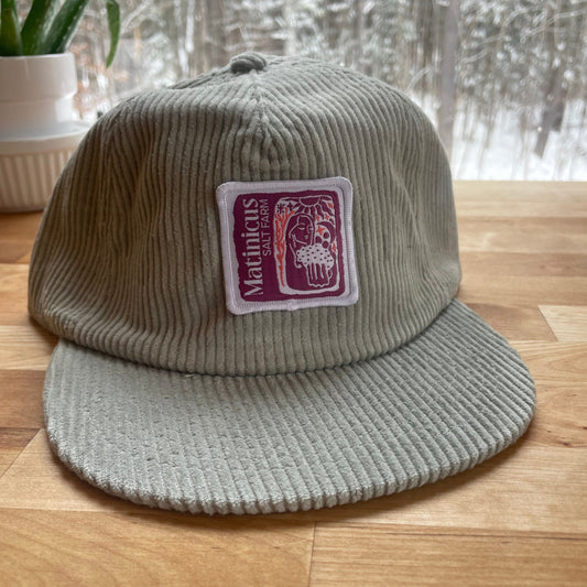 Gray corduroy cap with a plumb logo patch on a wooden surface