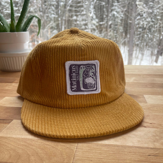 Yellow corduroy cap with an indigo logo patch on a wooden surface