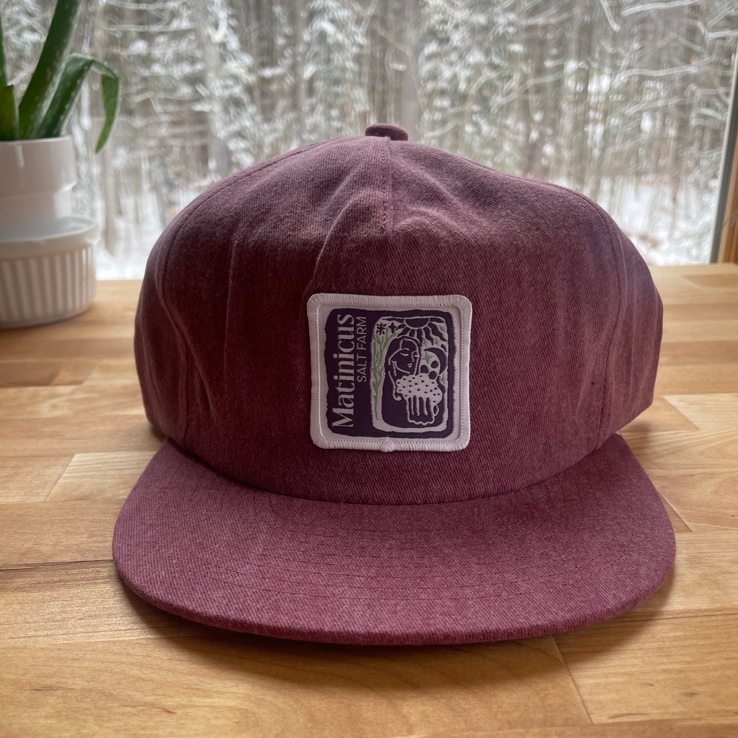 Maroon washed cotton cap with an indigo logo patch on a wooden surface
