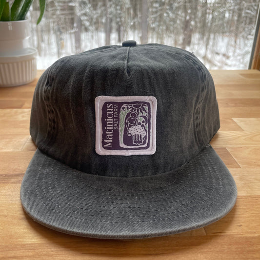 Black washed cotton cap with an indigo logo patch on a wooden surface