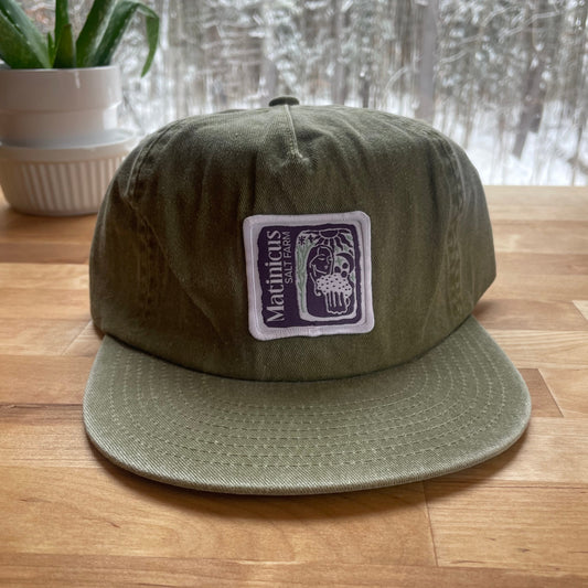 Green washed cotton cap with an indigo logo patch on a wooden surface