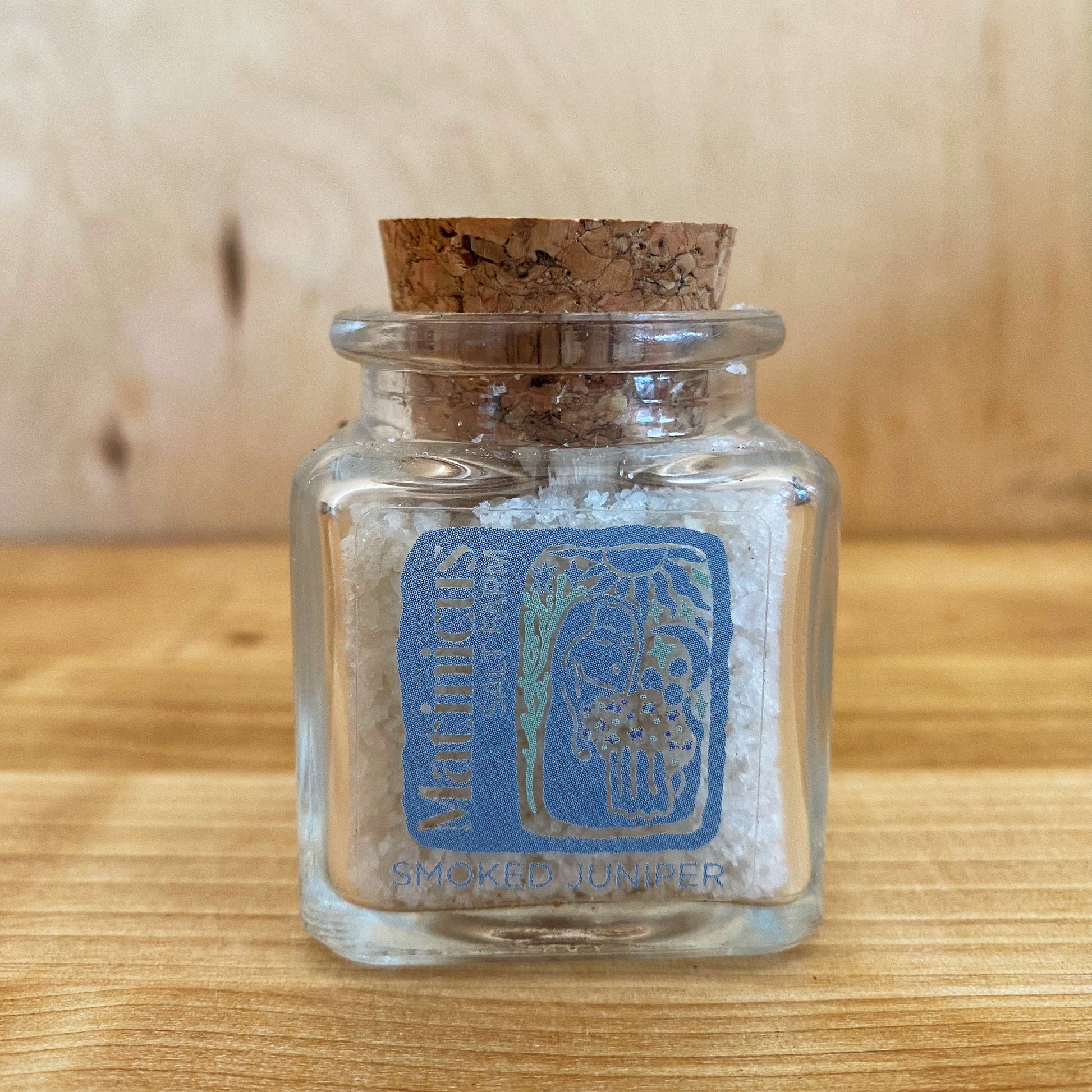 1.4 ounce glass jar containing smoked juniper sea salt with cork lid on a wooden surface